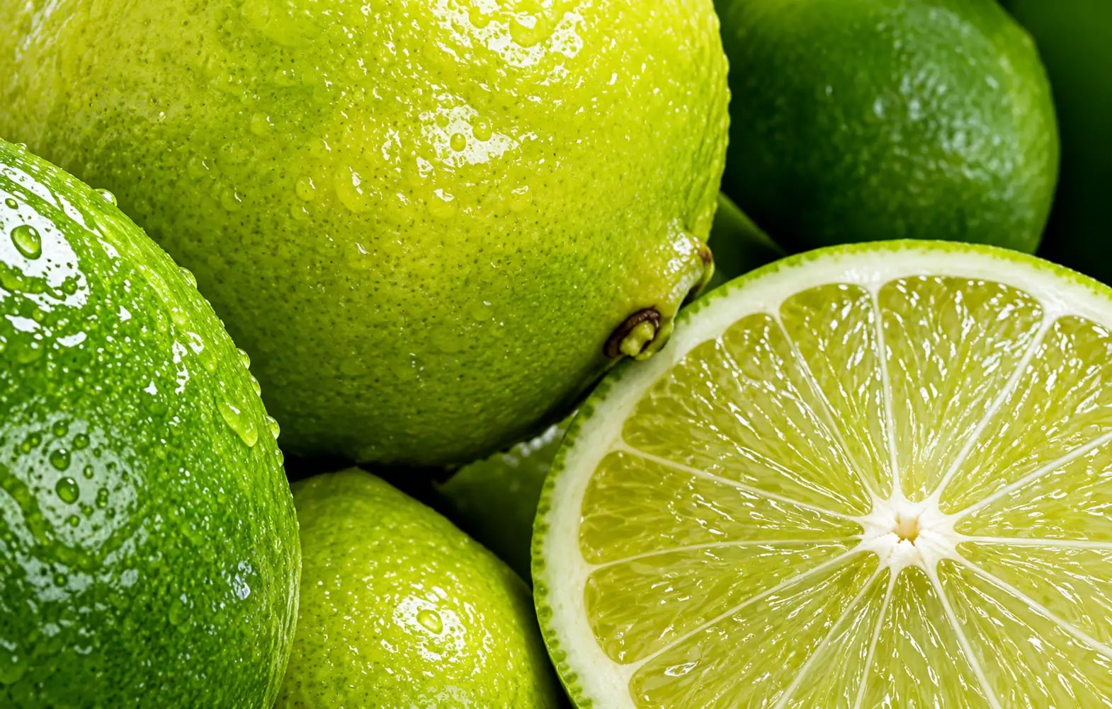 Close-up of glossy green lemons and a cut lime